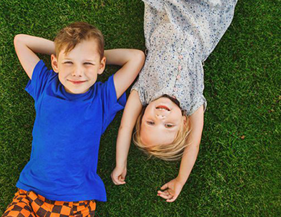 Two kids laying on a lawn